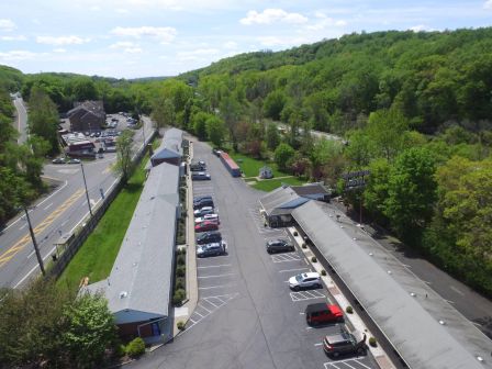 Aerial view of a small clustered office complex with long, single-story buildings, a parking lot, surrounding trees, and a road nearby.