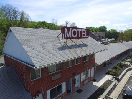 A brick motel with a large red &ldquo;MOTEL&rdquo; sign on the roof, a sloped gray roof, and a parking lot along the side.