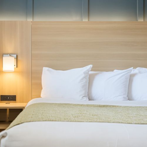 A clean hotel bed with white pillows and a warm bedside lamp, ready for a restful night.